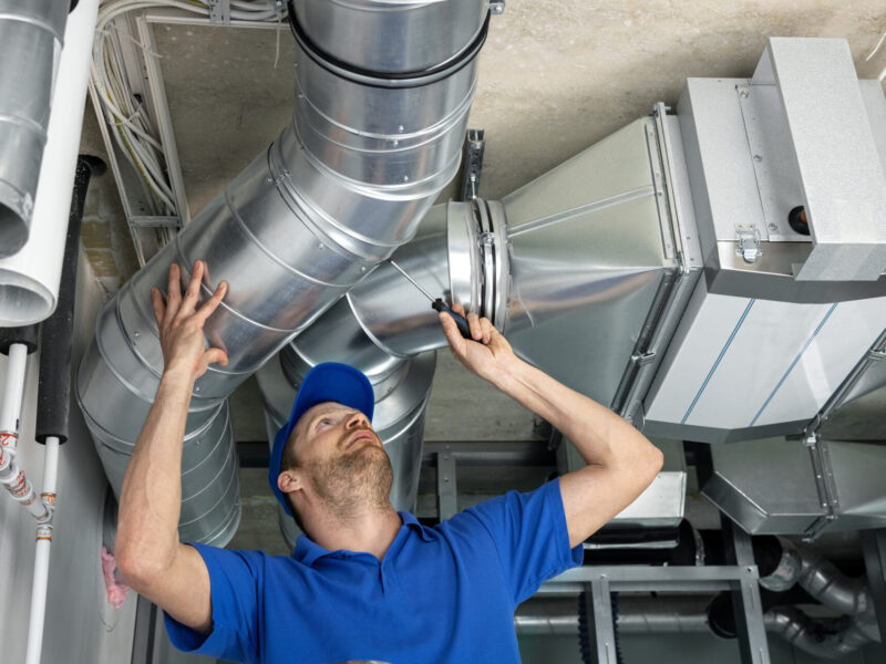 A man in a blue short-sleeved shirt and hat inspects shiny air ducts