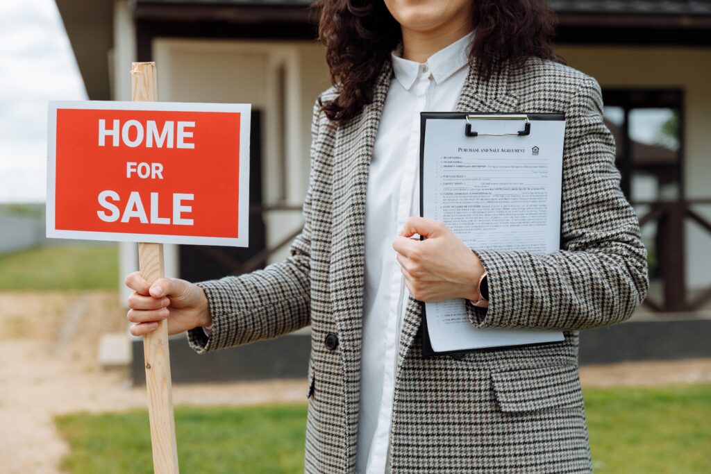 realtor holding for sale sign in front of an older home