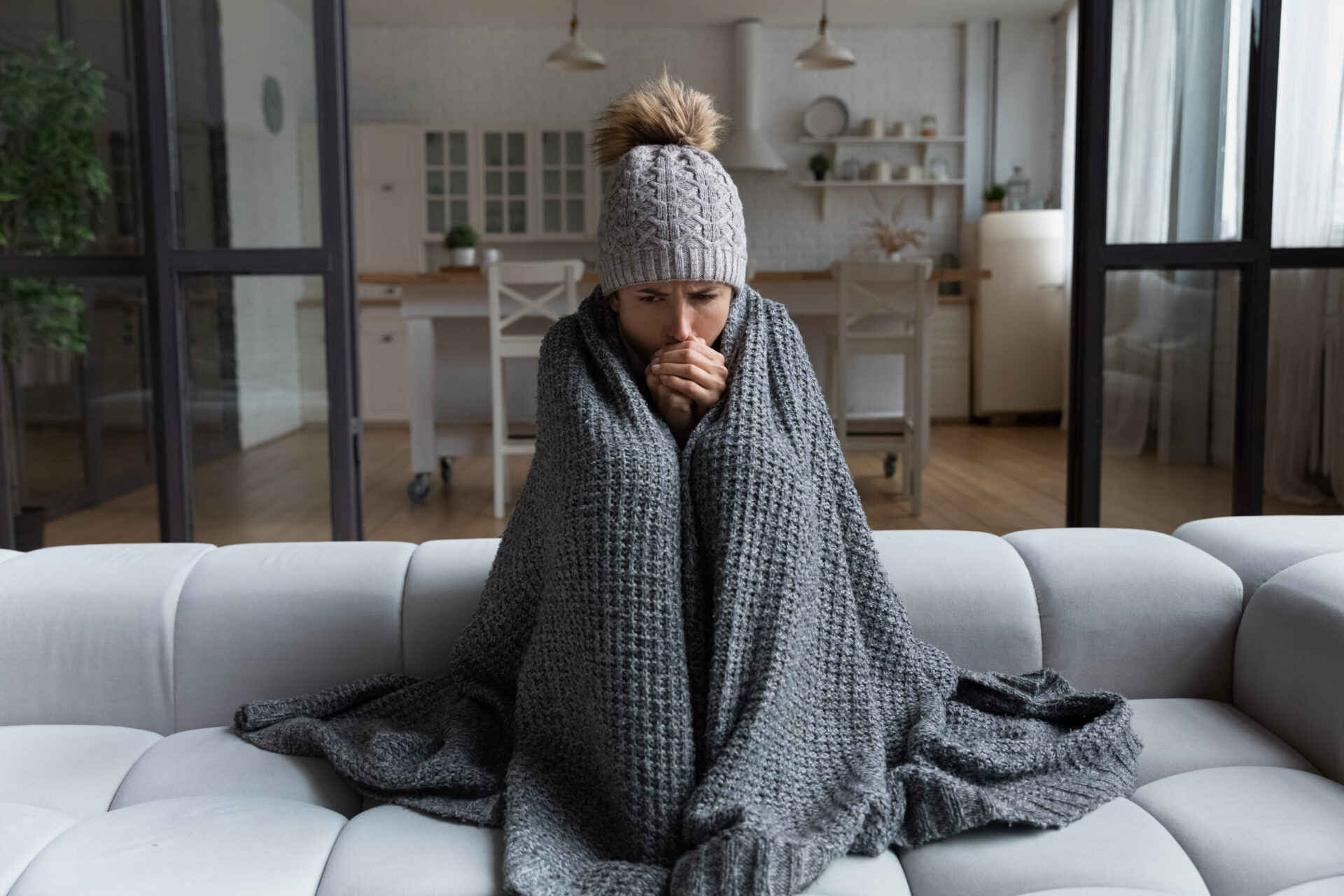 person wrapped in a gray blanket in a home that is still cold even with the heat on caused by drafts, poor insulation, and HVAC issues.