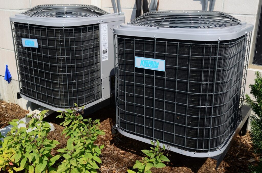 two central air conditioner outdoor units with wood chips and small plants