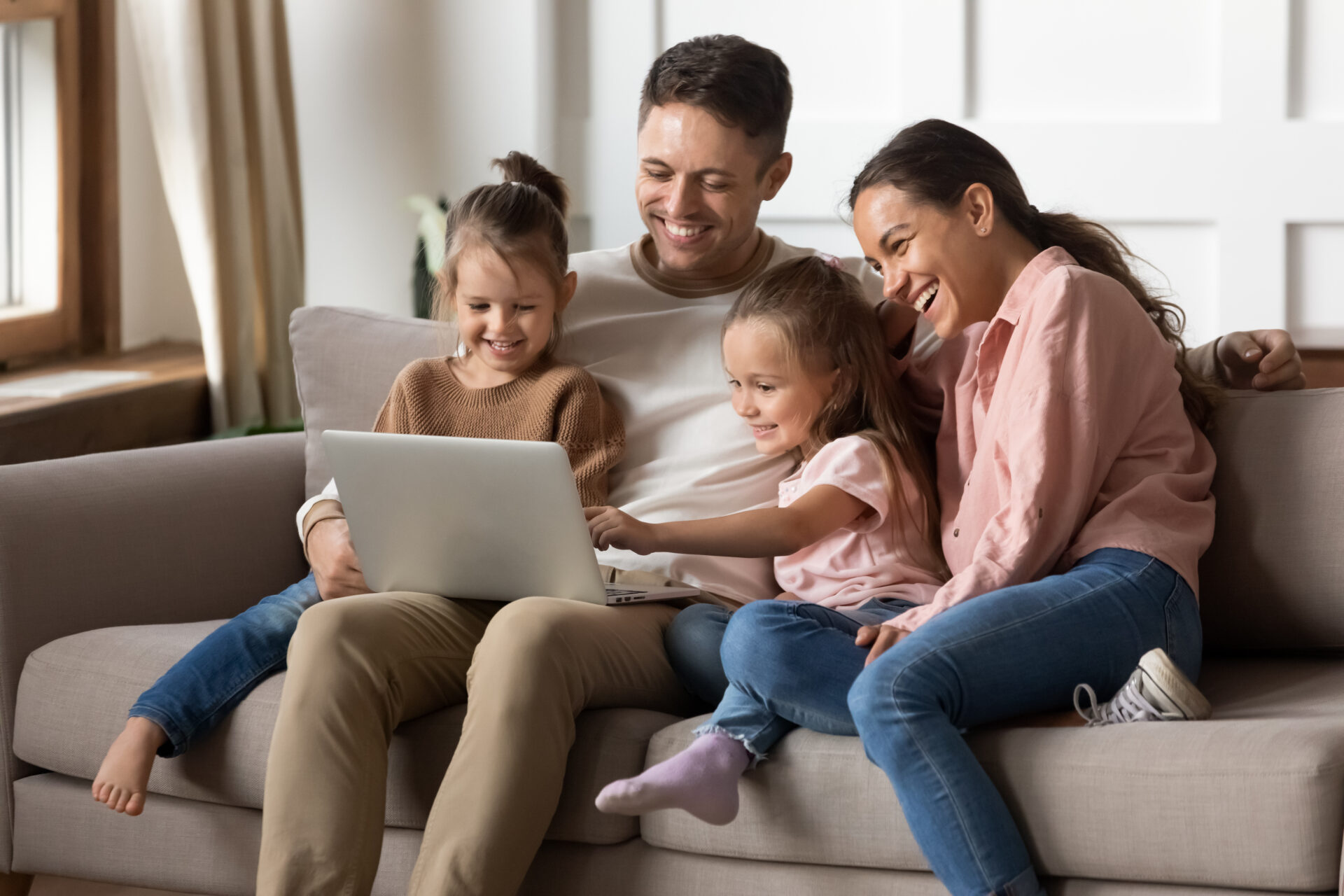 happy dark-haired family with two young kids smiling on a couch looking at a laptop screen