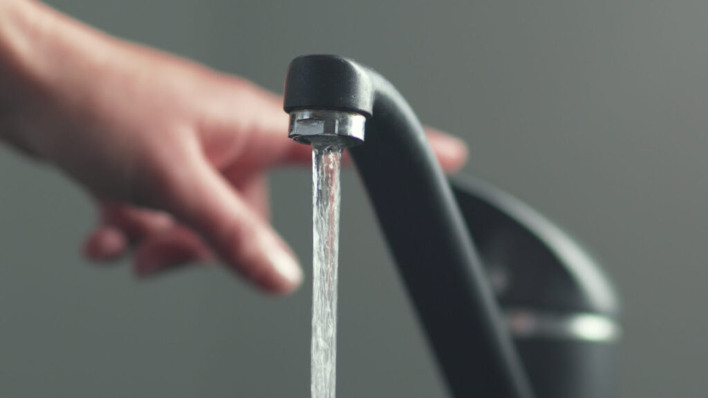 A close-up view of a hand turning the faucet to hot, which is made easier with on-demand hot water from a Rheem hot water heater