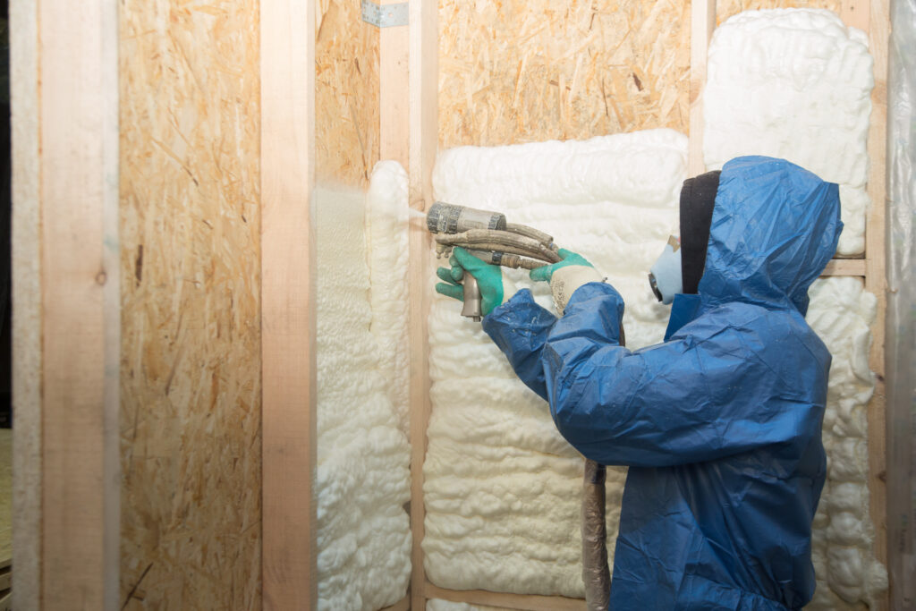 After consulting with the homeowner on which type of insulation is best, a technician in a blue protective suit applies spray foam insulation to an open wall cavity